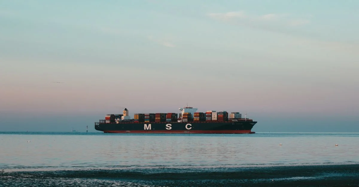 Un impressionnant navire cargo transportant des conteneurs à travers une mer tranquille sous un ciel pastel.