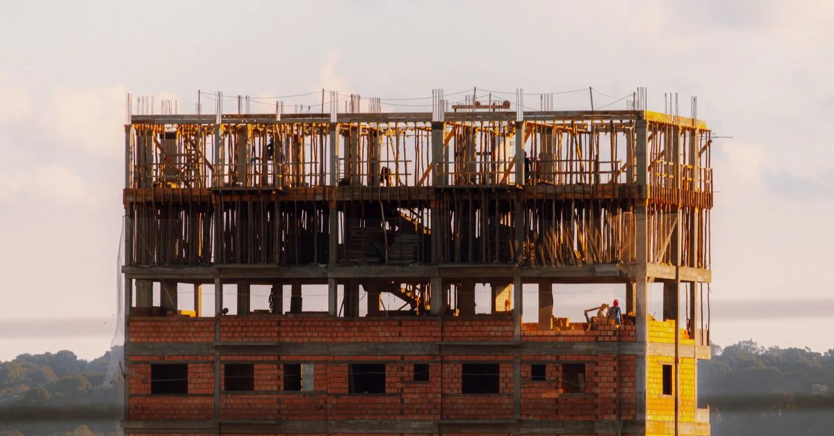 Bâtiment en briques en construction au coucher du soleil avec des travailleurs visibles au dernier étage.