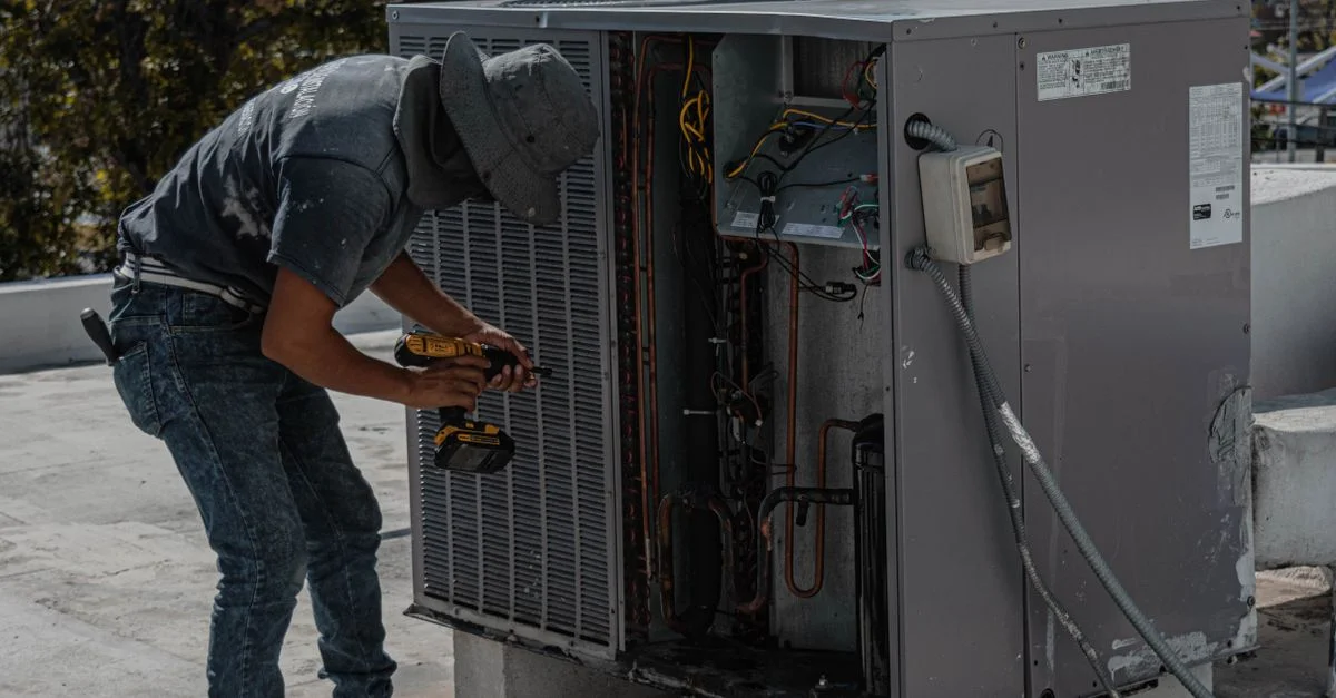 Un travailleur en chapeau de seau répare une unité de climatisation extérieure sur un toit.