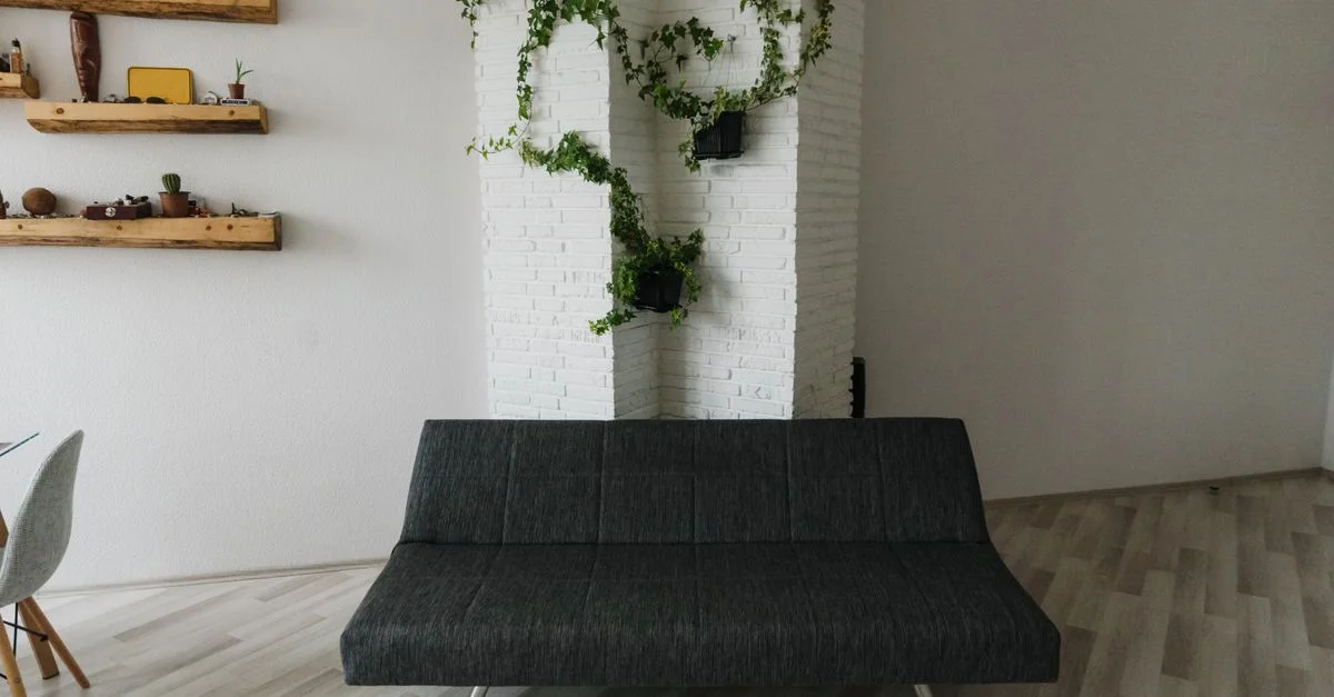 Salon contemporain avec un canapé gris foncé et des plantes décoratives sur un mur de briques blanches.
