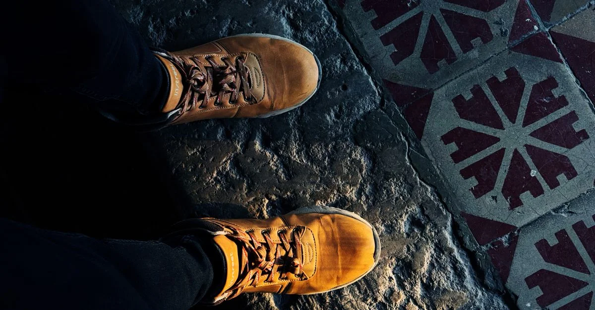 Vue de dessus de bottes marron sur un sol carrelé texturé à motifs géométriques.